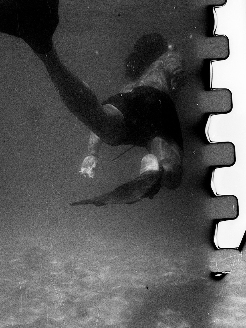 A grainy black and white image of a swimmer underwater 