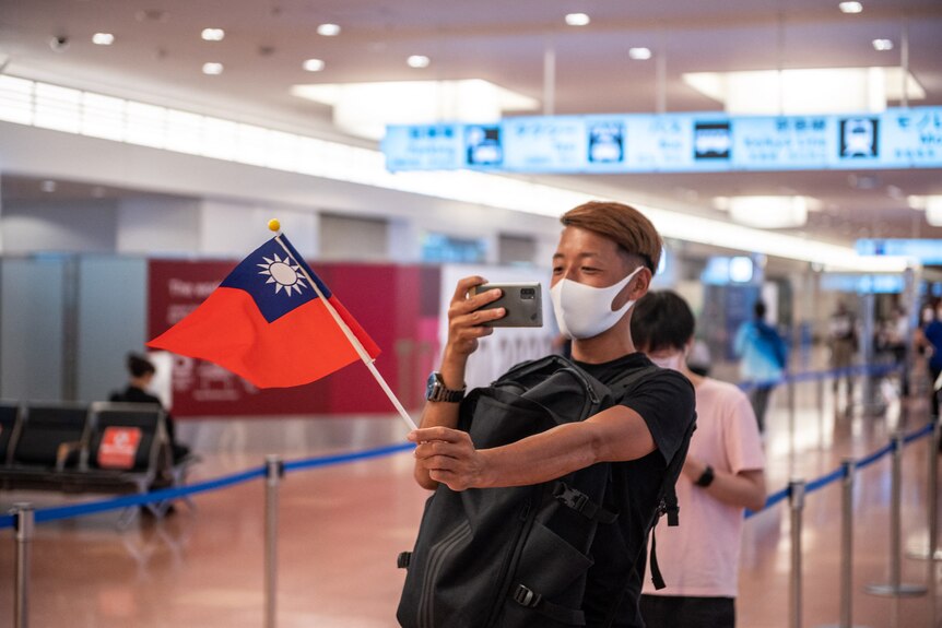 A young person in a mask leaning back and taking a photo of the Taiwanese flag at an airport.