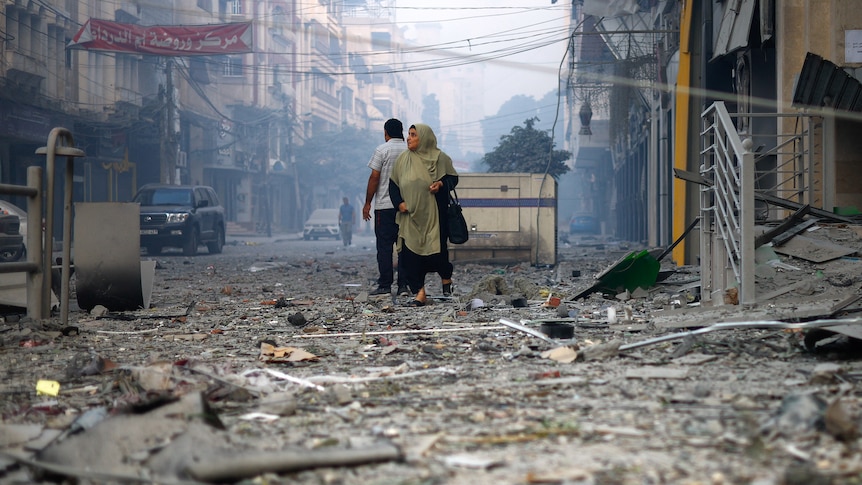 A woman looks on as she walks on a debris-strewn street.