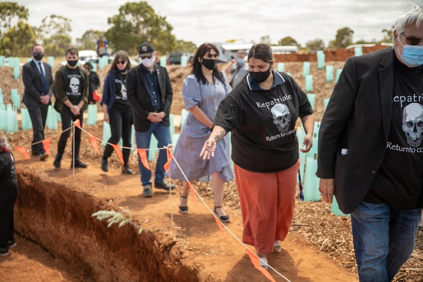 A line of people wearing black 'repatriate' shirts walk alongside the Kaurna burial ground