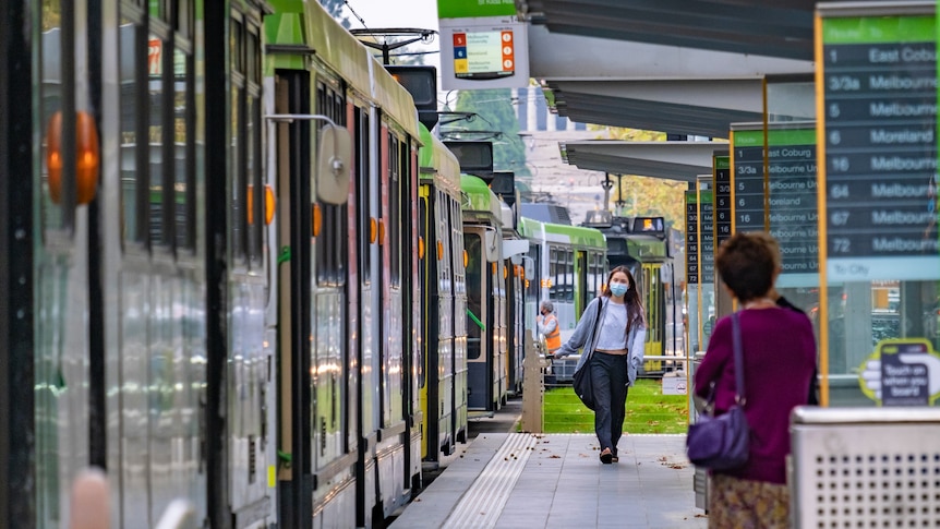 Two women stand on a tram platform in Melbourne's CBD.