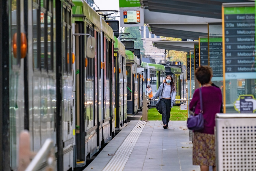 Two women stand on a tram platform in Melbourne's CBD.