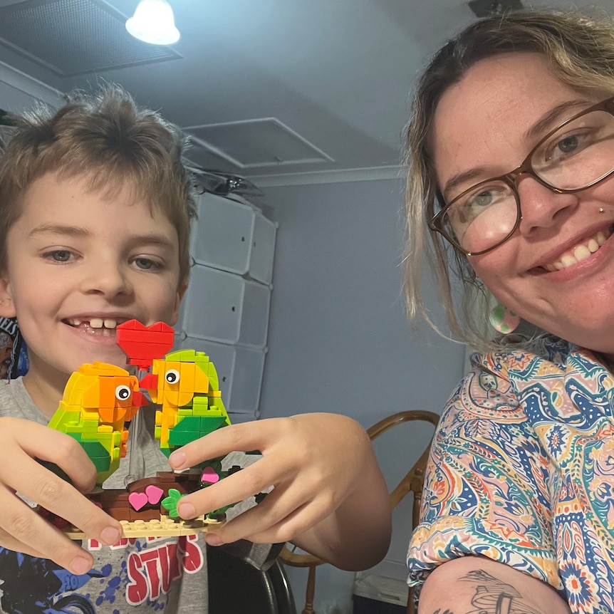 Kylie Hicklin smiling next to her son, who is also smiling and holding two birds made out of lego