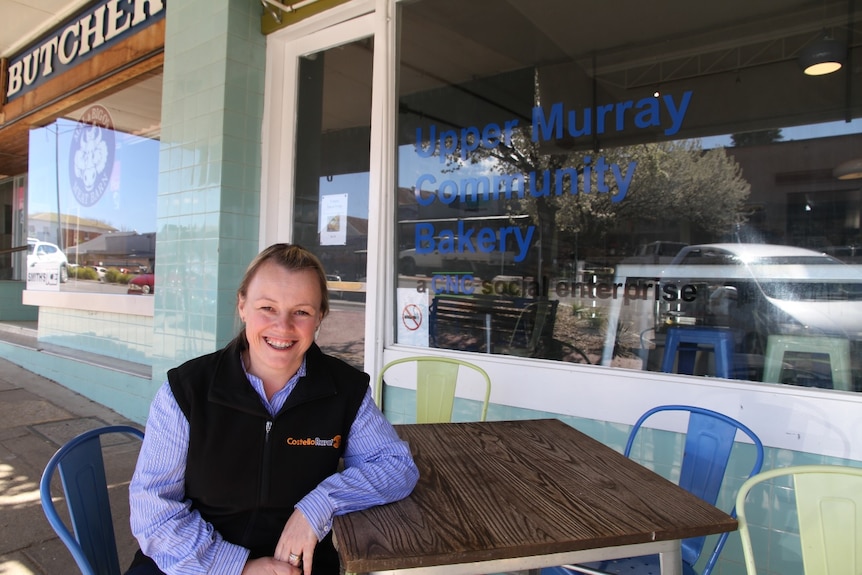 A woman sits outside of a bakery in the sun.