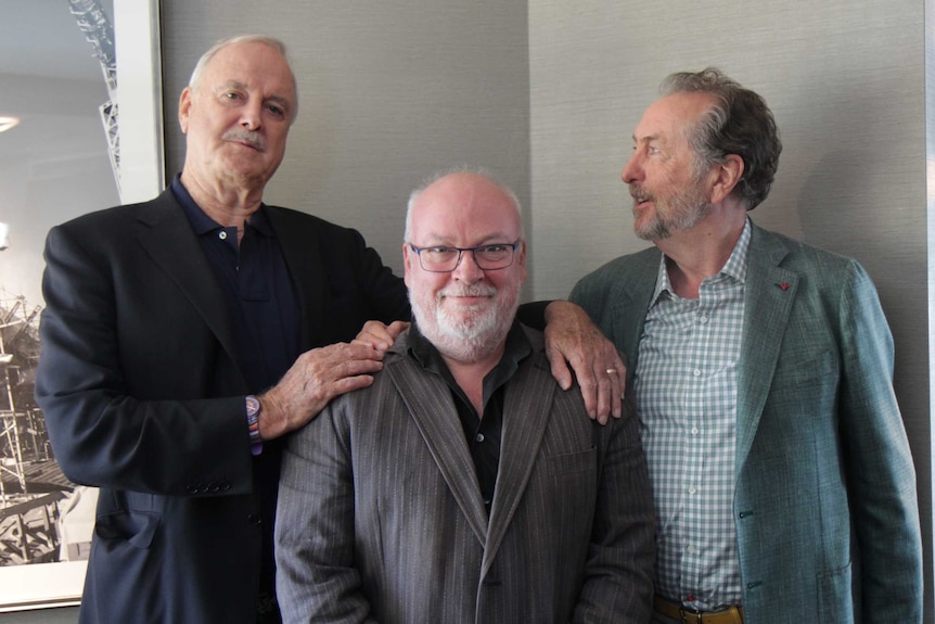 Ford standing between Cleese and Idle with arms around him.