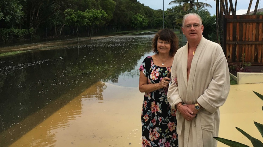 A woman and a man - the man wearing a robe - stand by a flooded road