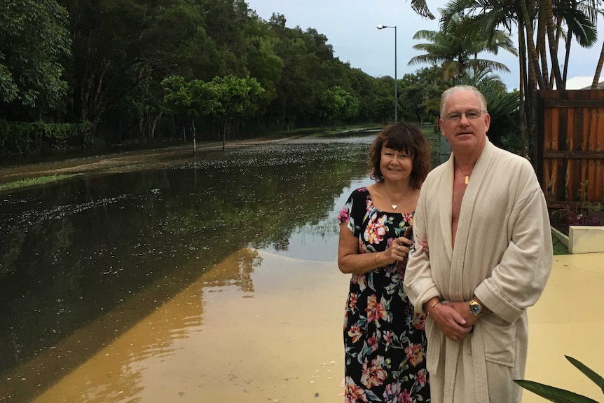 A woman and a man - the man wearing a robe - stand by a flooded road