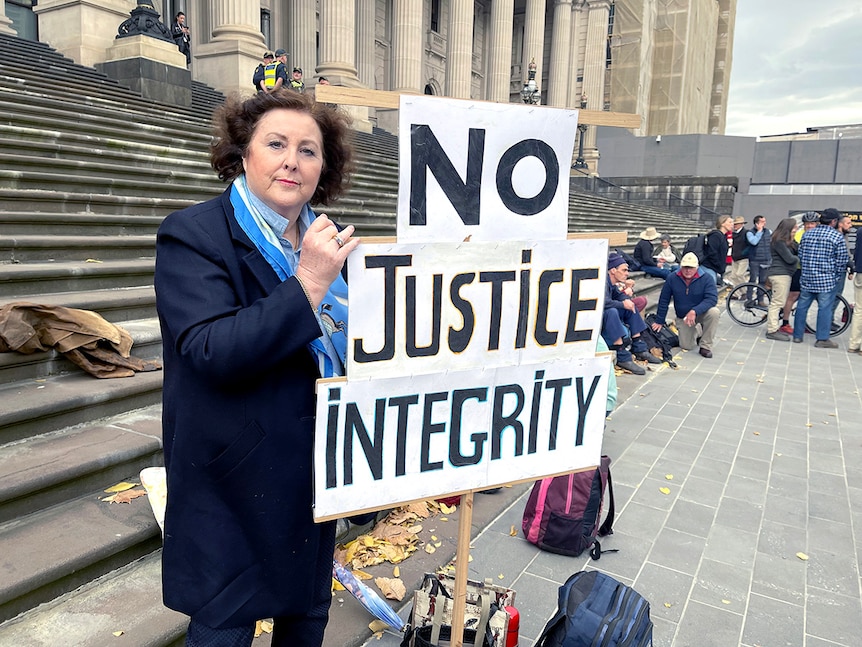 Lynne Riley stands on the steps of Parliament House with a placard which says 'no justice integrity'