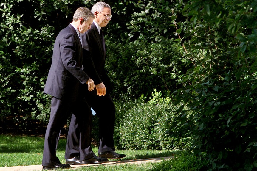 George W Bush and Colin Powell walk in the grounds of the White House.