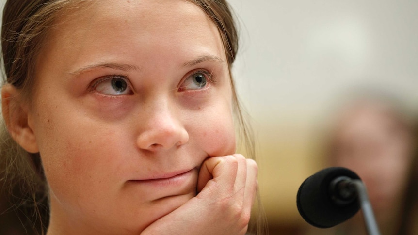Greta Thunberg looks upwards while resting her chin on her hand.
