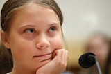 Greta Thunberg looks upwards while resting her chin on her hand.