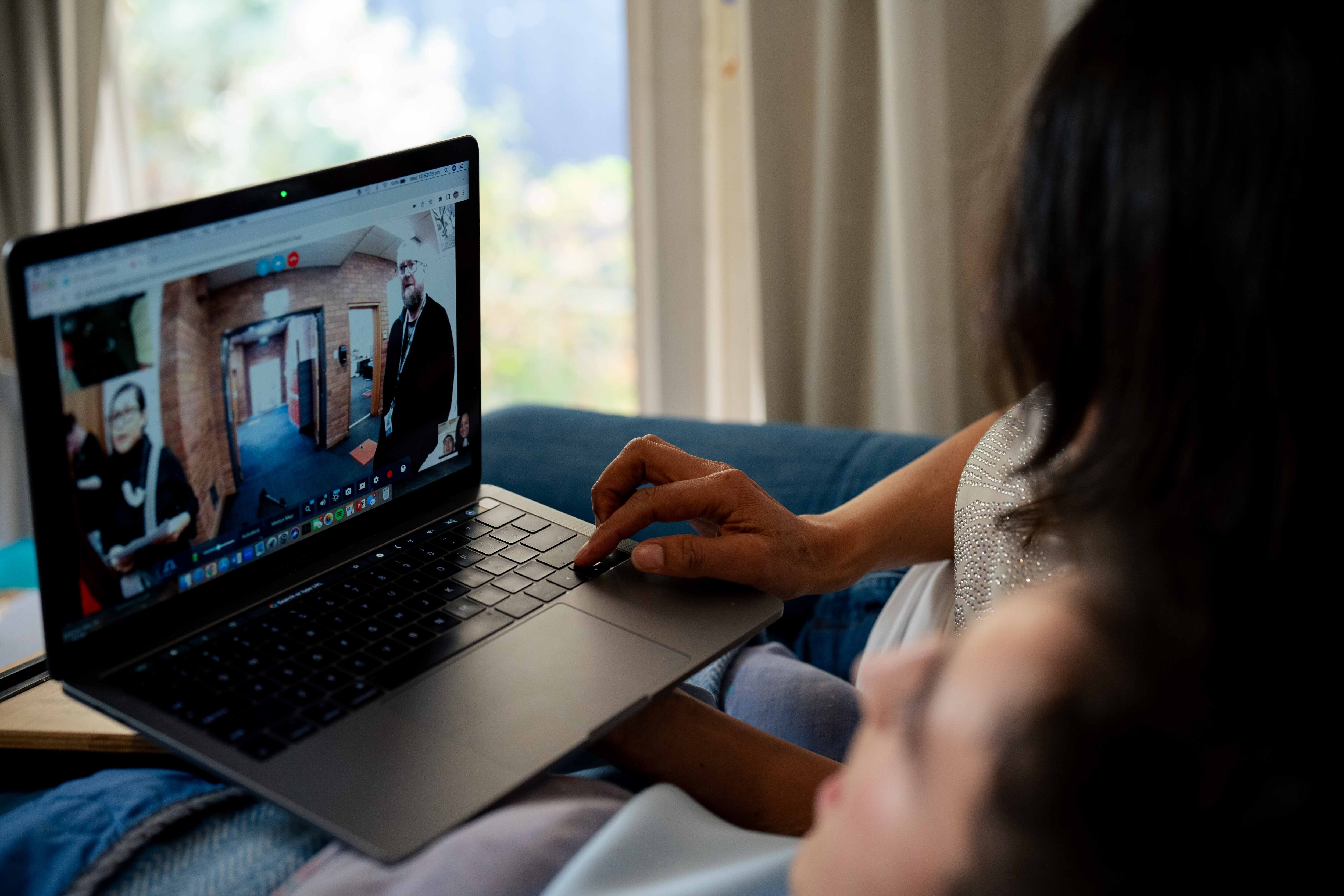 A laptop on a woman's lap with her son next to him.