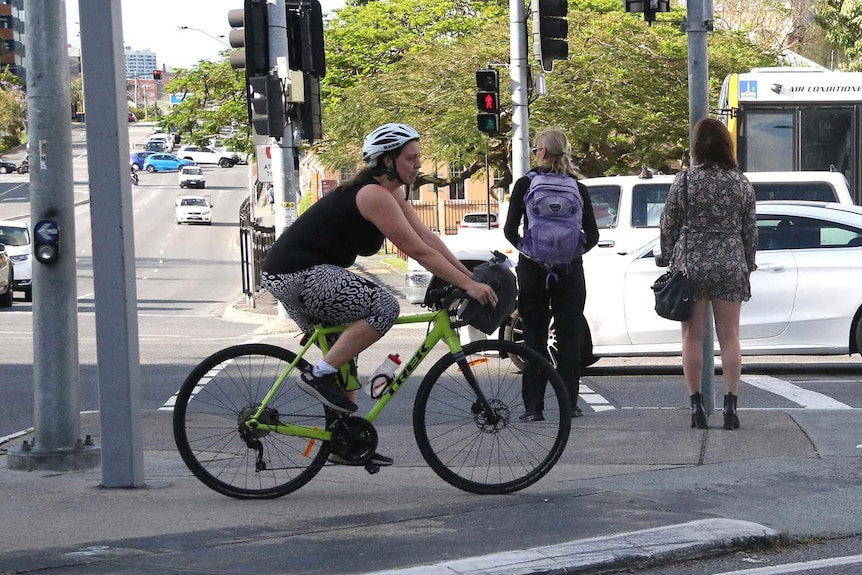 A woman on a bicycle on a pedestrian traffic island in the middle of a busy road
