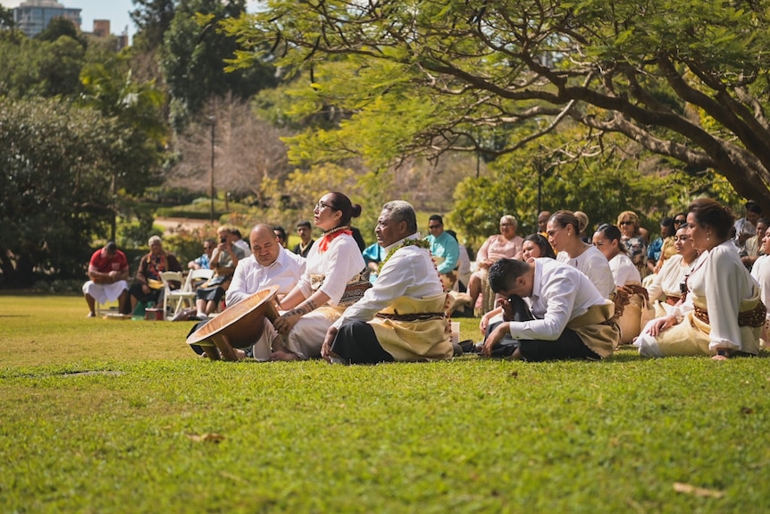 Tongan community sit on grass in a park as part of a ceremony.