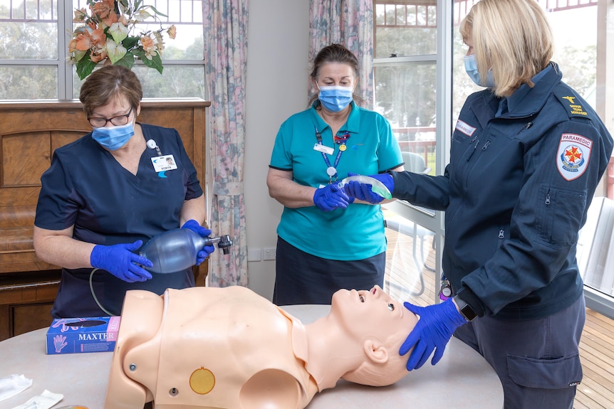 Three women stand around a dummy