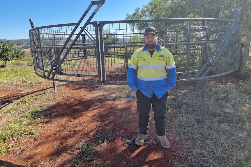Wide shot of a man in high vis gear standing in front of a large circular pig trap.