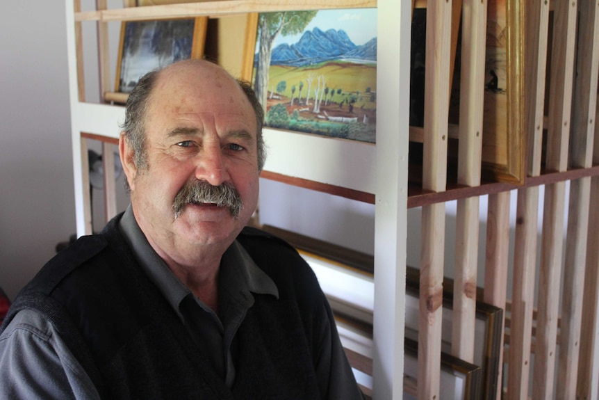 Albany man, Tony Davis, in front of shelves containing the work of renowned Noongar artist, Bella Kelly.