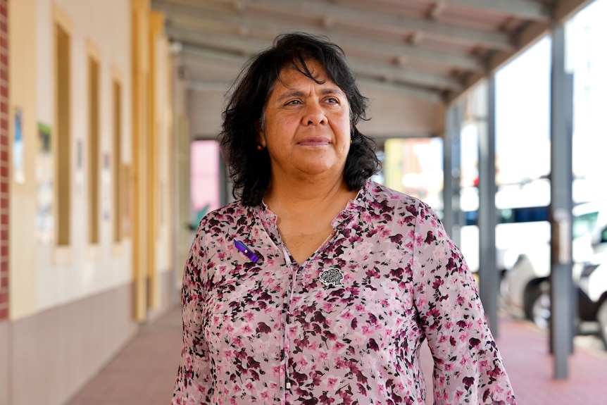 An Aboriginal woman wearing a pink and purple shirt standing in the middle of the footpath. 
