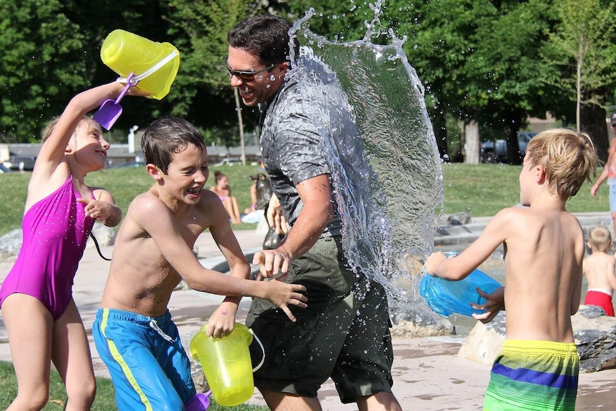 Man and children playing with water at the park to show family time as a benefit of shift work
