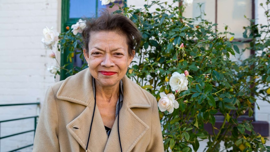 A woman stands in front of a rose bush