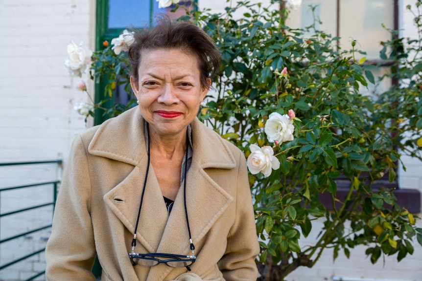 A woman stands in front of a rose bush