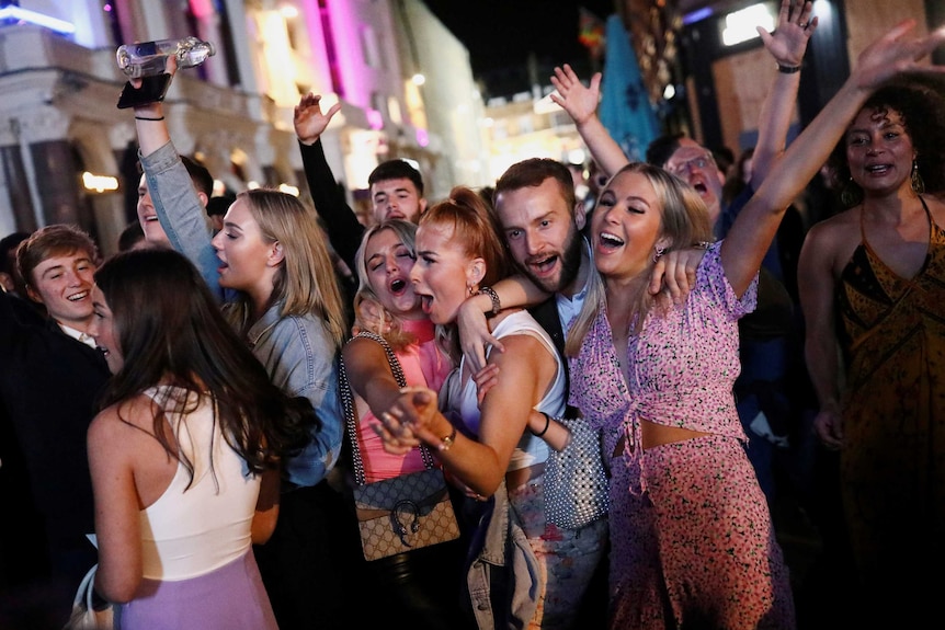 A group of young people dancing and hugging in the street at night