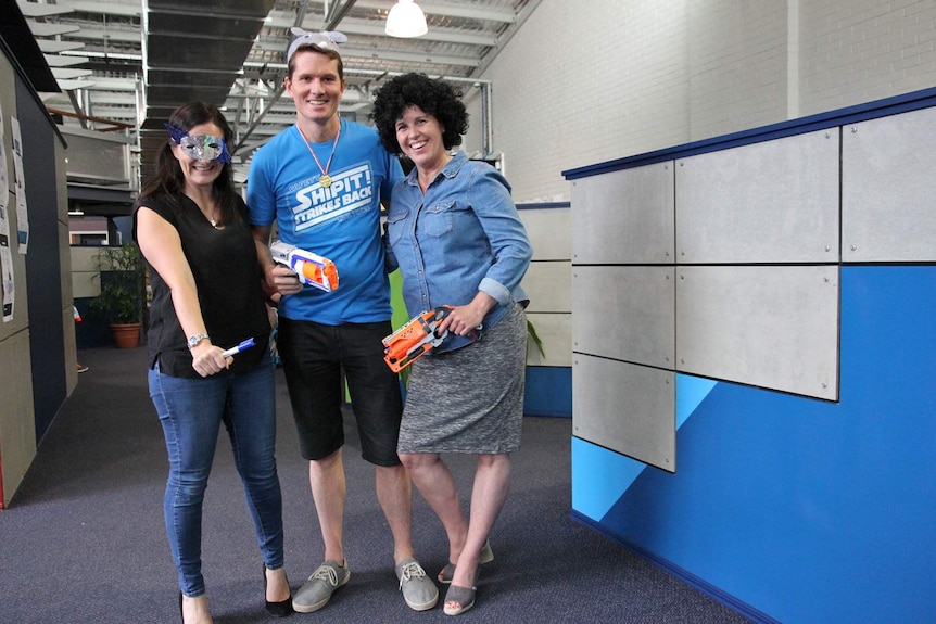 Two women and one man stand holding Nerf guns in an office space