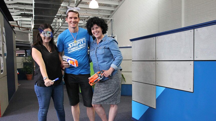 Two women and one man stand holding Nerf guns in an office space