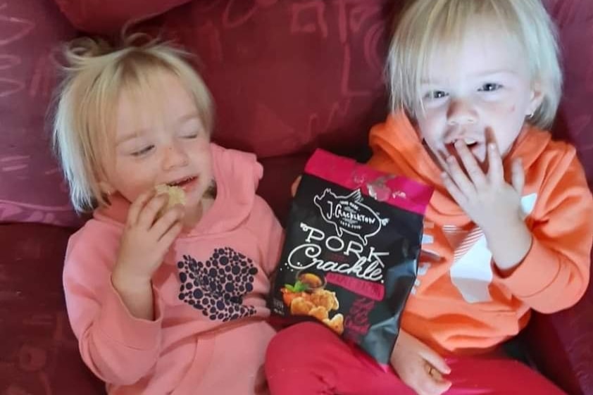 two toddler girls on a couch eating from a bag of chips