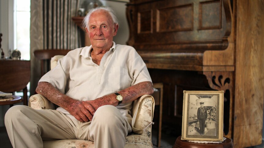 David Manning, 93, at home in Ballarat sitting on an armchair with a picture of him as a young 13-year- old in navy attire.