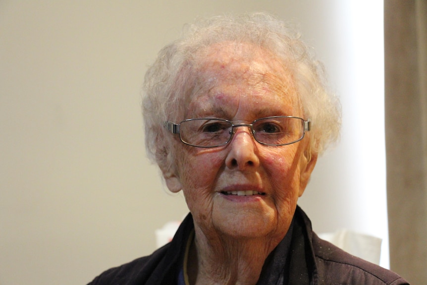 A woman with white hair and glasses smiles at the camera.
