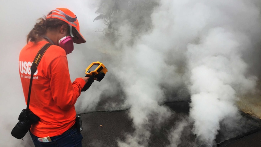 Geologist inspects a crack in Hawaii. She is wearing a gas mask, there is a lot of gas coming out of the fissure.