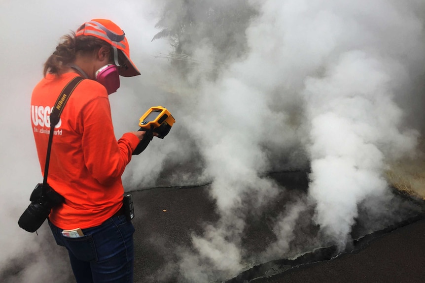 Geologist inspects a crack in Hawaii. She is wearing a gas mask, there is a lot of gas coming out of the fissure.