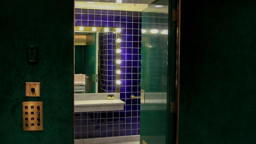 A photo of doorway into a bathroom with royal blue tiles and a vanity with dressing room lights