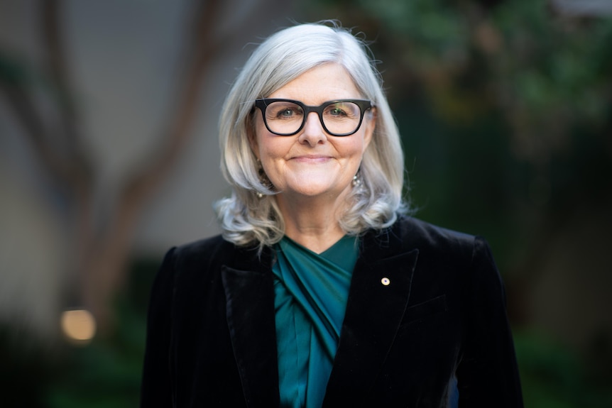 Sam Mostyn smiles while standing in a courtyard