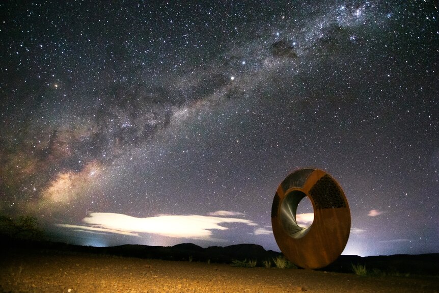 A donut-shaped sculpture underneath a very starry night sky, showing the Milky Way