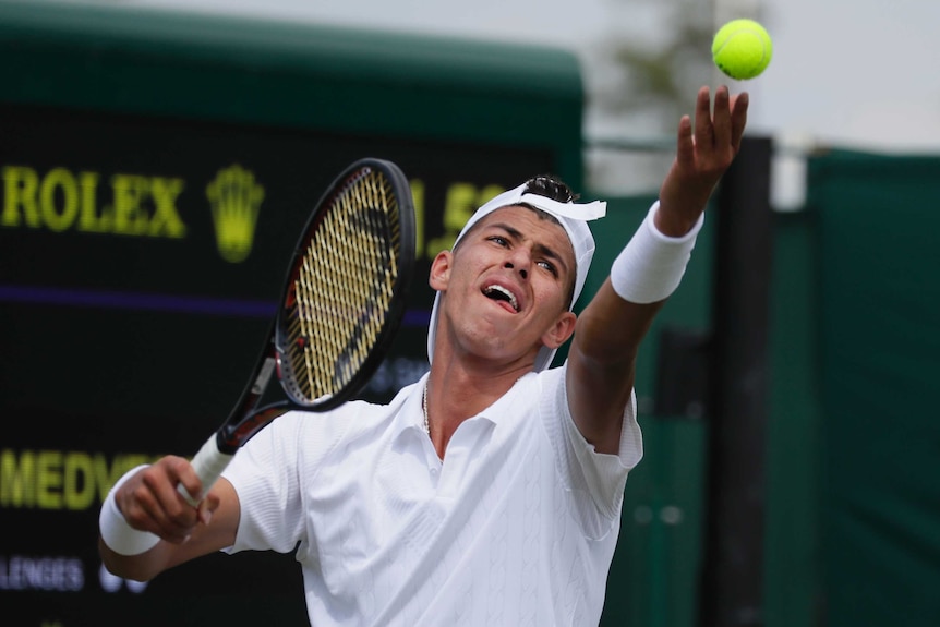 Alexei Popyrin stares at the ball he has tossed as he prepares to serve.