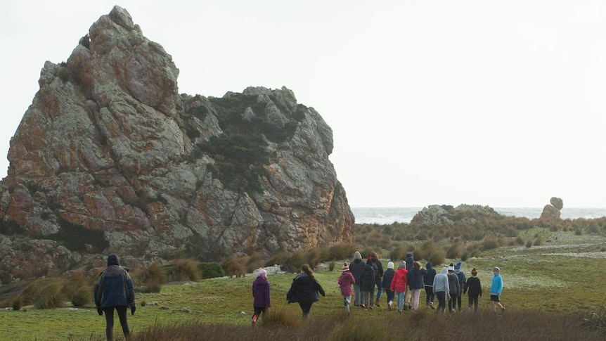 School group walks past huge rocky landmark