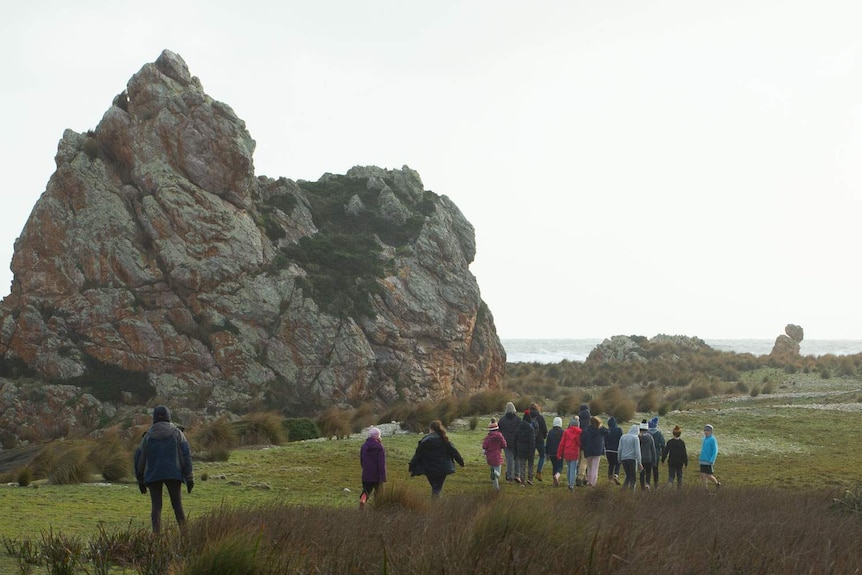 School group walks past huge rocky landmark