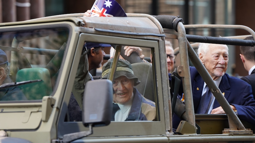 Some elderly men are driven in an army vehicle.