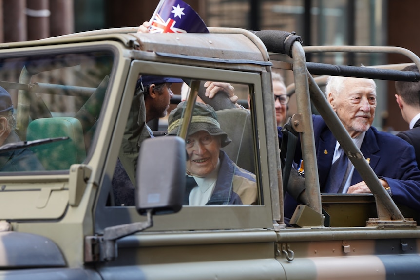 Some elderly men are driven in an army vehicle.