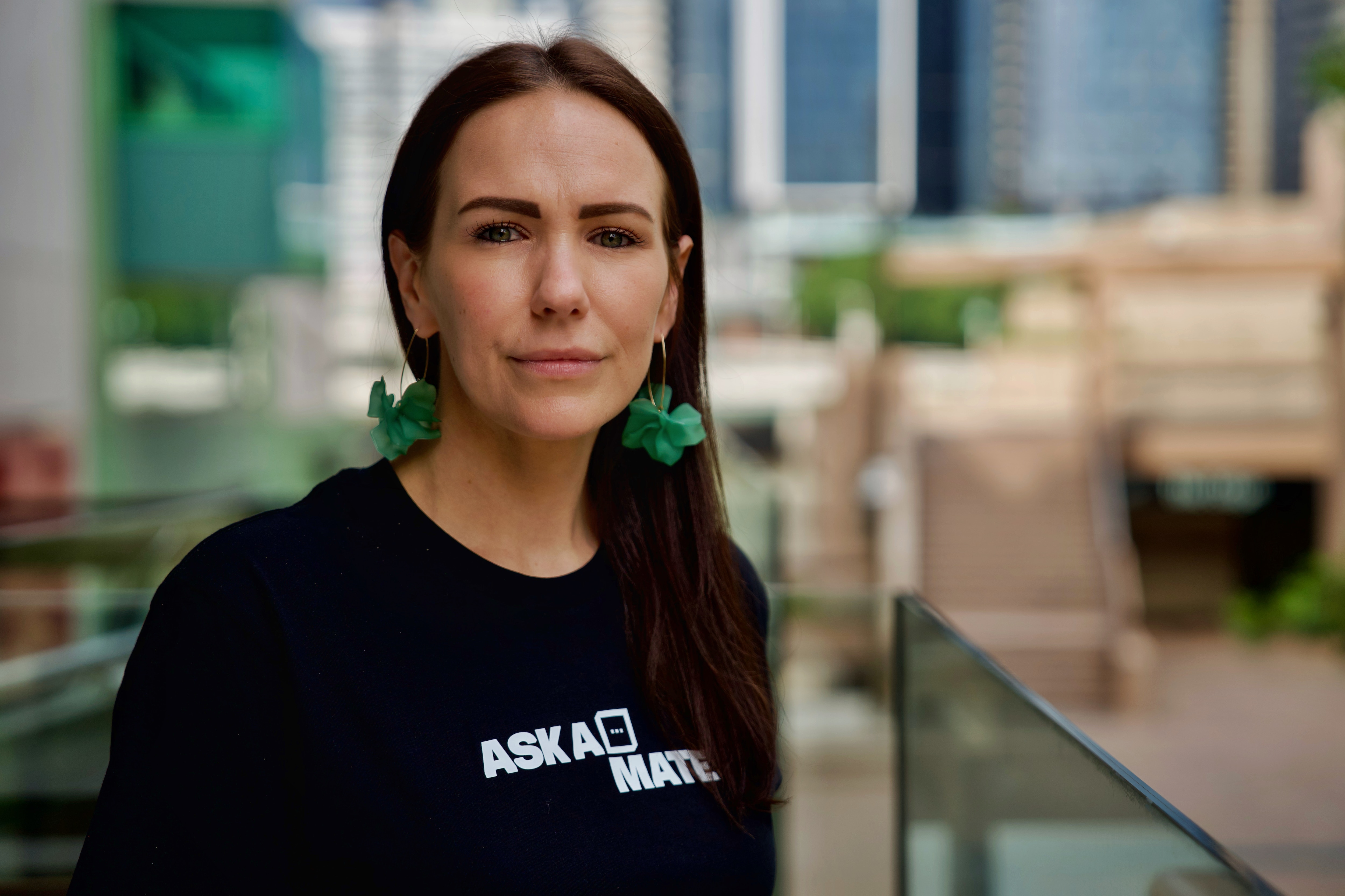 Uma mulher de cabelo castanho escuro usa brincos verdes e uma camisa preta que diz: Pergunte a um parceiro.