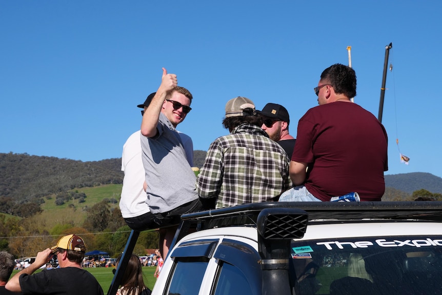 One man gives a thumbs up while he and his group watch the football from the roof of a car
