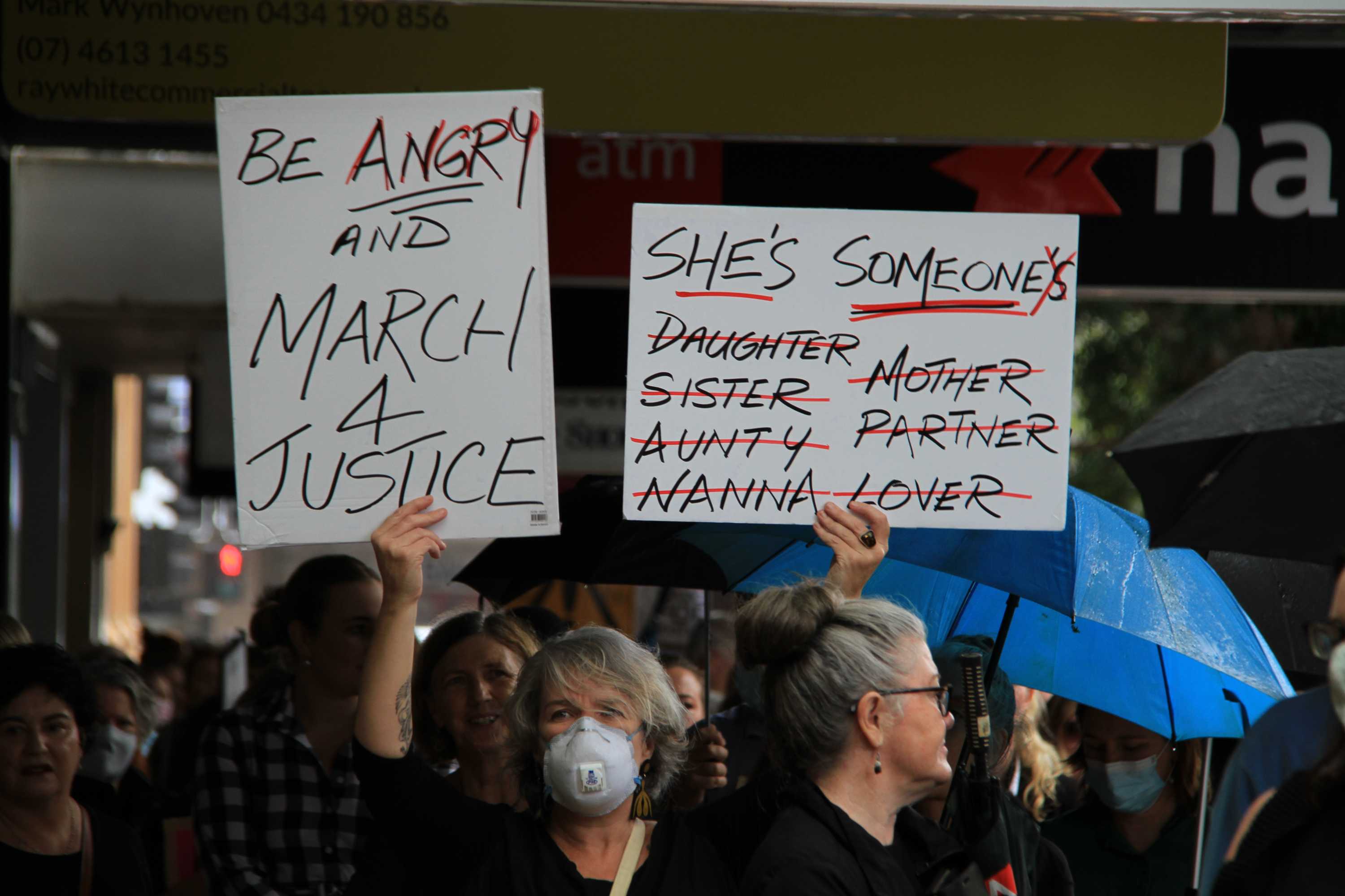 A women wearing a mask holds a sign at the March 4 Justice event.