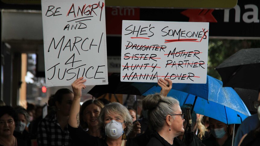 A women wearing a mask holds a sign at the March 4 Justice event.