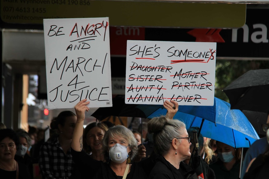 A women wearing a mask holds a sign at the March 4 Justice event.