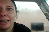 A close-up of a woman sitting in a 4WD vehicle, with floodwater at a high level visible out the window behind her.