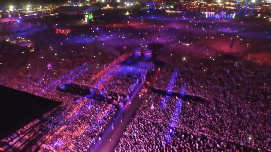 A giant crowd at a festival, bathed in purple light