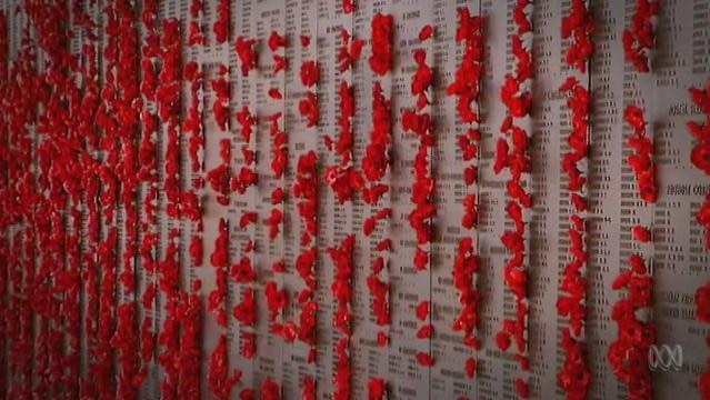 Red poppies inserted into wall of names at War Memorial