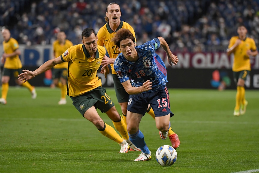 A Japanese footballer runs toward goal with the ball, as an Australian defender tries to intercept him in a World Cup qualifier.